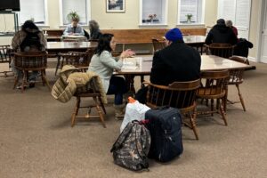 People sit at a series of tables, where volunteers help people fill out questionnaires