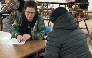 A woman seated at a table and speaking to a man as she fills out a questionnaire