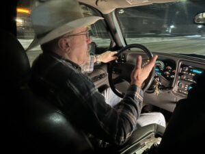 A man wearing a flannel shirt and cowboy hat driving a truck