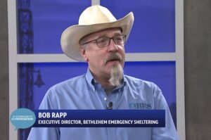 Bob Rapp wearing a blue shirt and white cowboy hat, speaking at the PBS39 news set